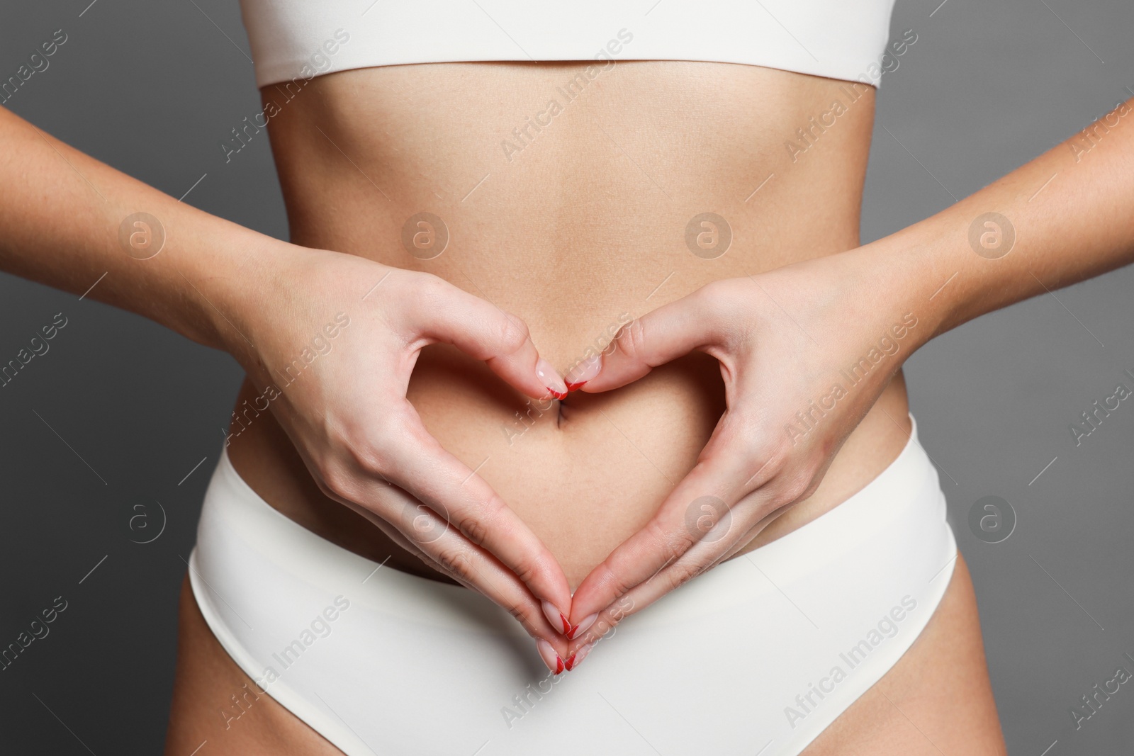Photo of Young woman with flat belly making heart gesture on grey background, closeup