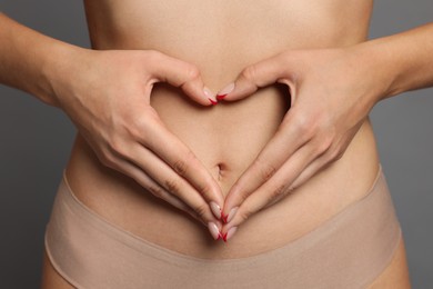 Photo of Young woman with flat belly making heart gesture on grey background, closeup
