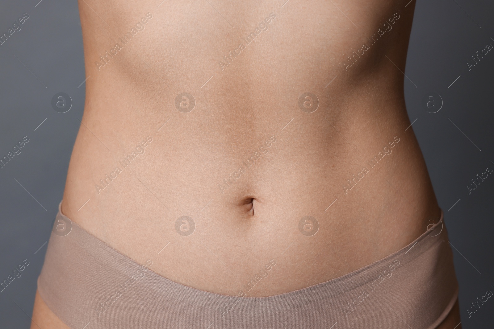 Photo of Young woman with flat belly on grey background, closeup