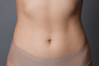 Photo of Young woman with flat belly on grey background, closeup