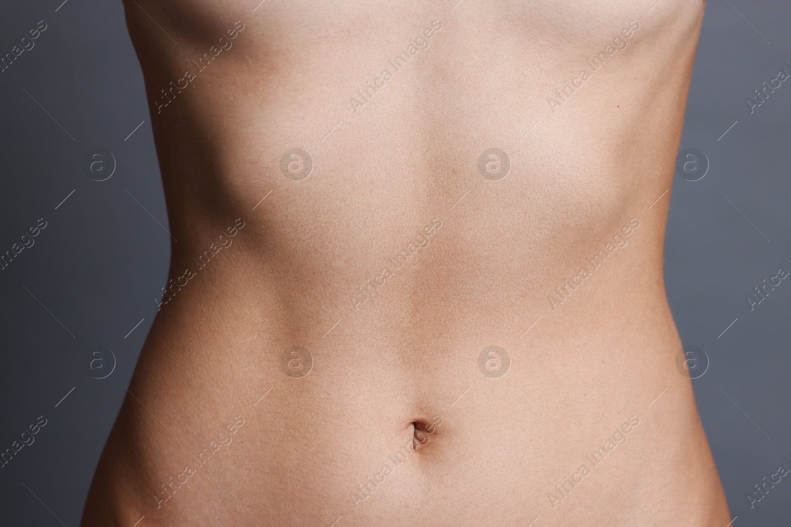 Photo of Young woman with flat belly on grey background, closeup