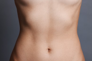 Photo of Young woman with flat belly on grey background, closeup