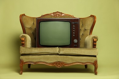 Photo of Retro TV set and sofa on olive background. Used stuff