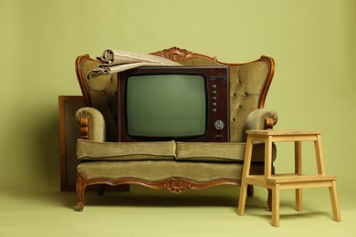 Photo of Retro TV set, sofa, step stool and rug on olive background. Used stuff