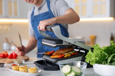 Photo of Man cooking vegetables and meat on electric grill in kitchen, closeup