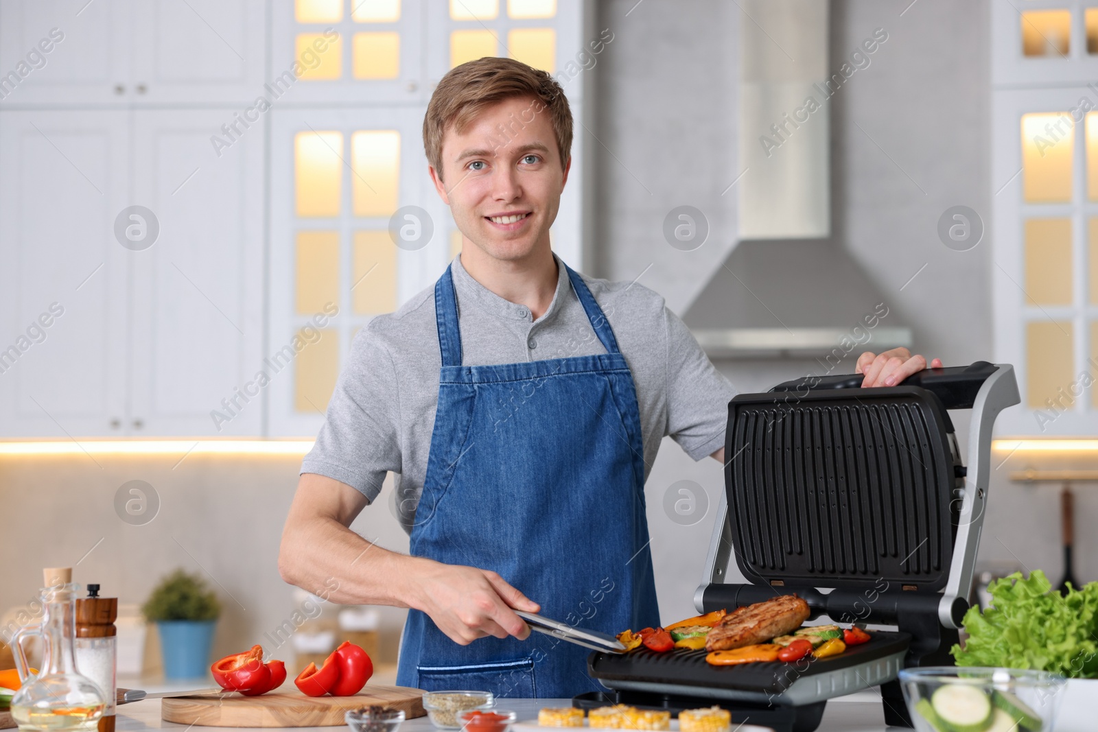 Photo of Man cooking vegetables and meat on electric grill in kitchen