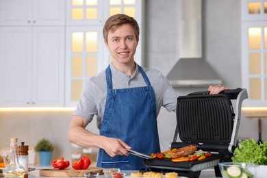 Photo of Man cooking vegetables and meat on electric grill in kitchen