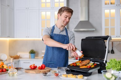 Photo of Man adding salt to vegetables and meat cooking on electric grill in kitchen