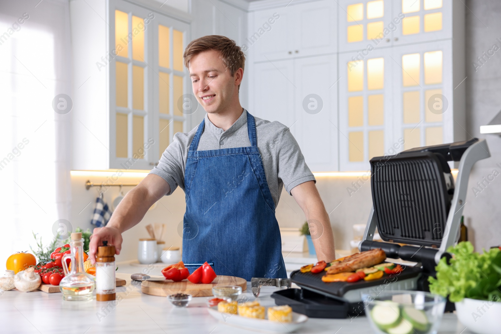 Photo of Man cooking vegetables and meat on electric grill in kitchen