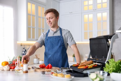 Photo of Man cooking vegetables and meat on electric grill in kitchen