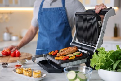 Photo of Man cooking vegetables and meat on electric grill in kitchen, closeup