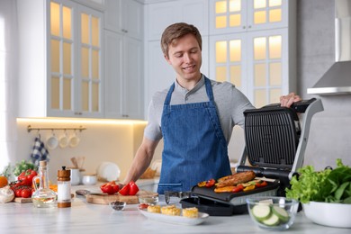 Photo of Man cooking vegetables and meat on electric grill in kitchen