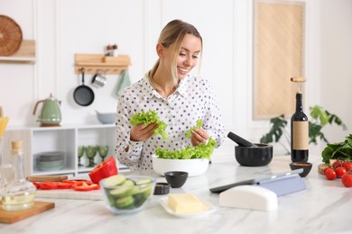 Photo of Smiling woman looking at recipe on tablet while cooking at table in kitchen