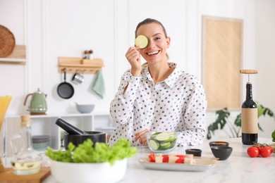 Photo of Portrait of smiling woman with slice of zucchini cooking at table in kitchen
