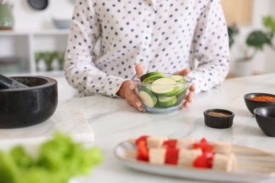 Photo of Woman with slices of zucchini cooking at marble table in kitchen, closeup