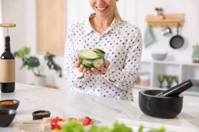Photo of Smiling woman with slices of zucchini cooking at table in kitchen, closeup