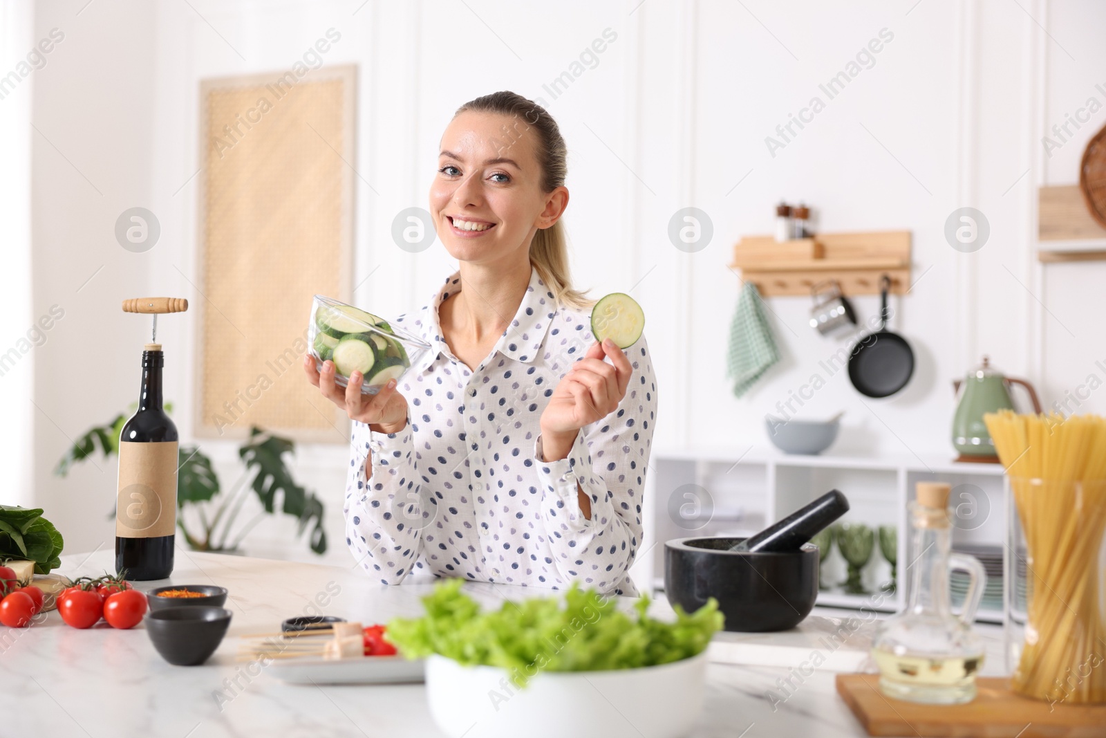 Photo of Portrait of smiling woman with slices of zucchini cooking at table in kitchen