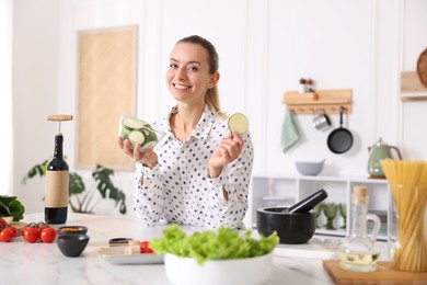 Photo of Portrait of smiling woman with slices of zucchini cooking at table in kitchen