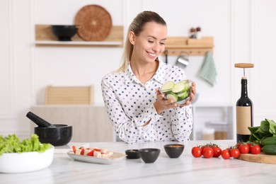 Photo of Smiling woman with slices of zucchini cooking at table in kitchen