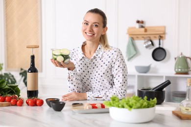 Photo of Smiling woman with slices of zucchini cooking at table in kitchen