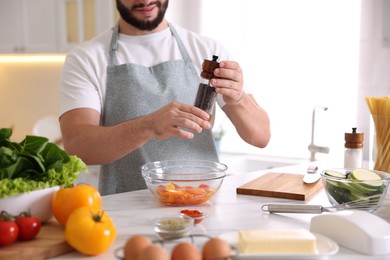 Photo of Cooking process. Smiling man seasoning dish at table in kitchen, closeup