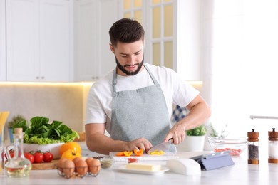 Photo of Cooking process. Young man cutting bell pepper at table in kitchen