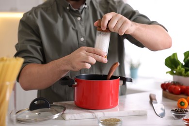 Photo of Cooking process. Man seasoning dish at table indoors, closeup
