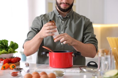 Photo of Cooking process. Man seasoning dish at table indoors, closeup