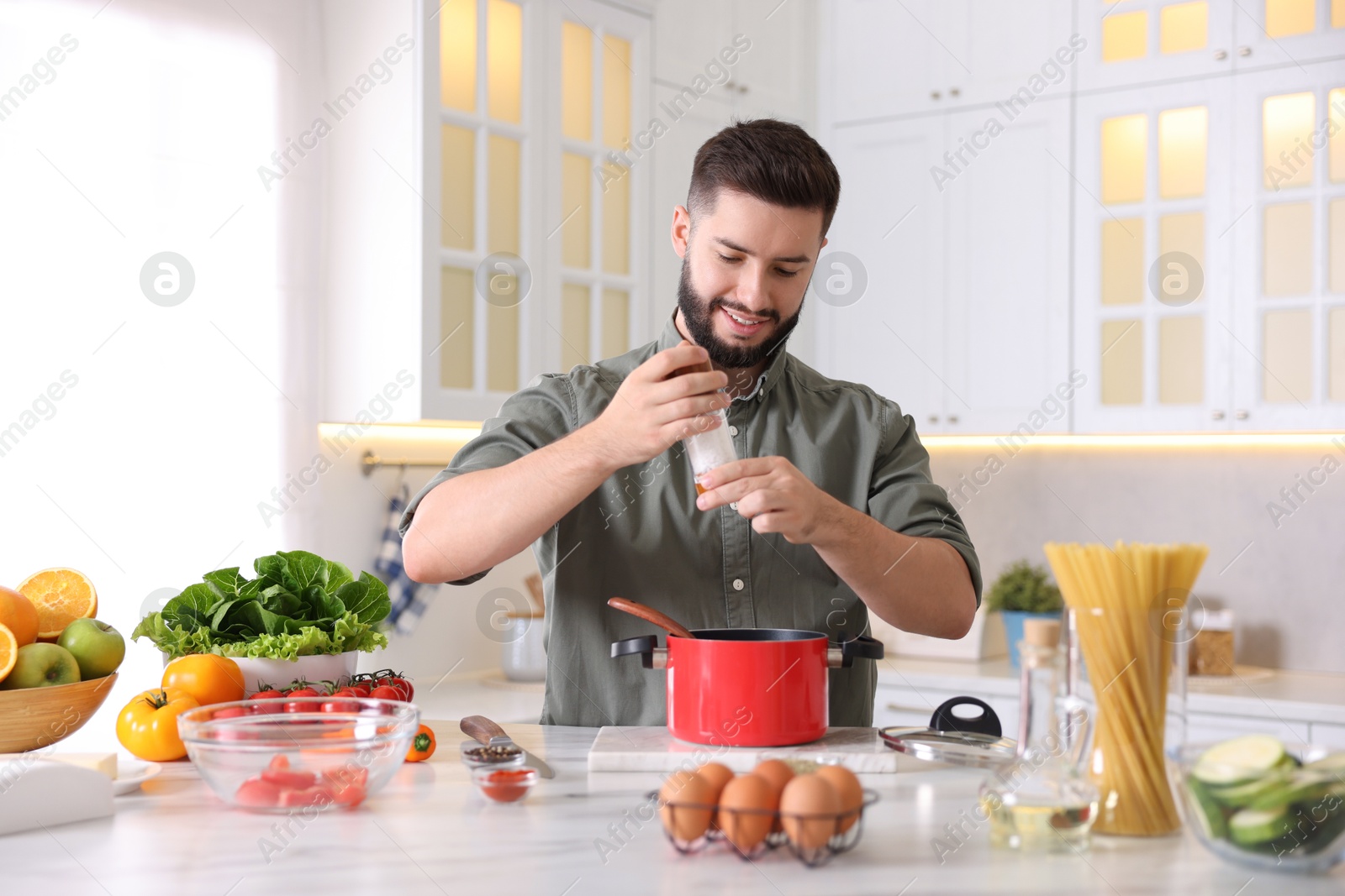Photo of Cooking process. Smiling man seasoning dish at table in kitchen