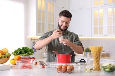 Photo of Cooking process. Smiling man seasoning dish at table in kitchen