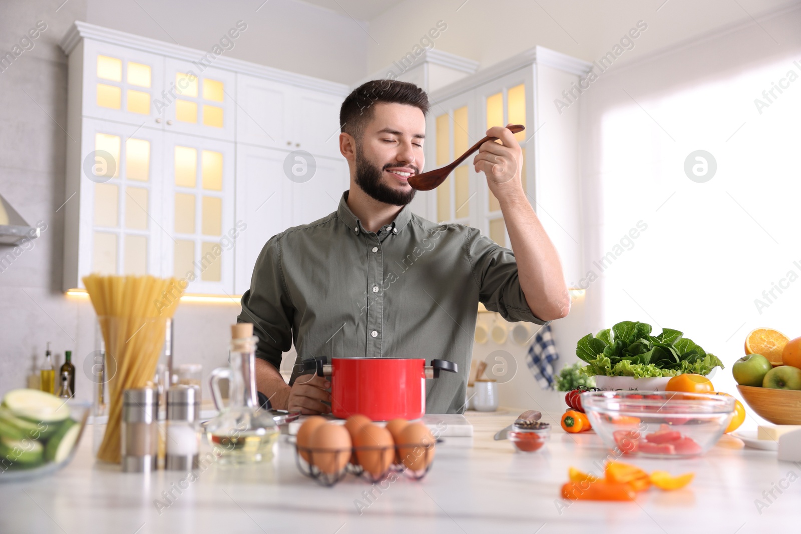 Photo of Smiling man tasting meal after cooking at table in kitchen