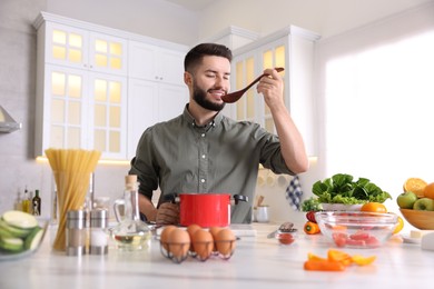 Photo of Smiling man tasting meal after cooking at table in kitchen