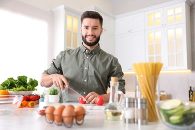 Photo of Cooking process. Smiling man cutting tomato at table in kitchen
