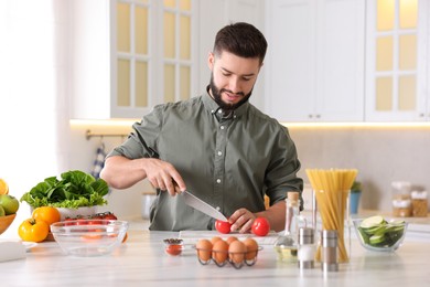 Photo of Cooking process. Smiling man cutting tomato at table in kitchen