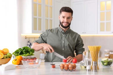 Photo of Cooking process. Smiling man cutting tomato at table in kitchen