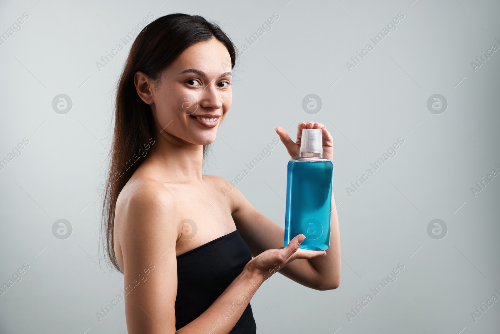 Photo of Smiling young woman with bottle of mouthwash on grey background. Oral hygiene