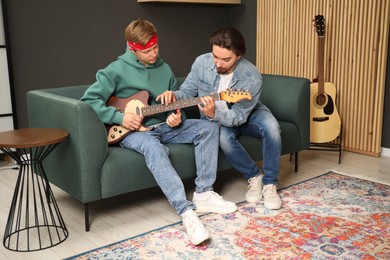 Photo of Tutor teaching man to play guitar on sofa indoors