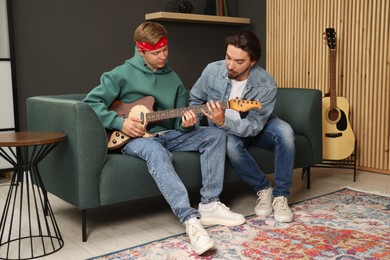 Photo of Tutor teaching man to play guitar on sofa indoors