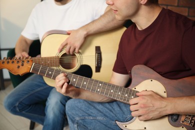 Photo of Tutor teaching man to play guitar at home, closeup