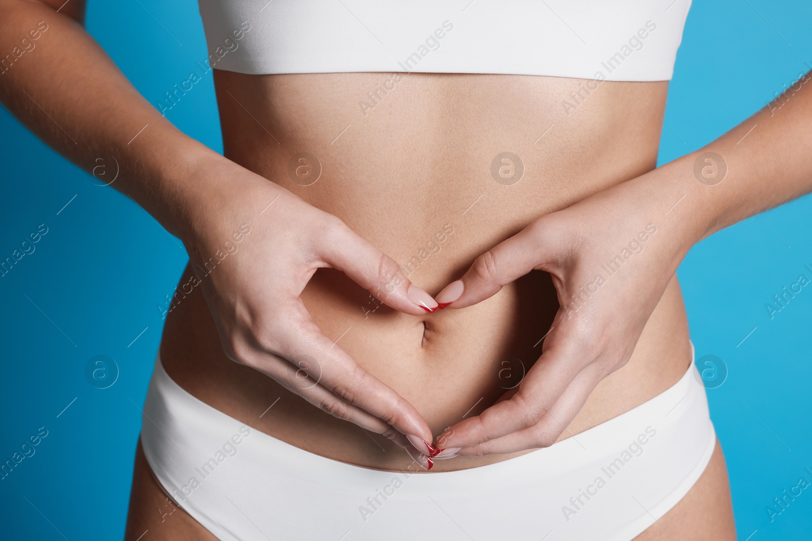 Young woman with flat belly making heart gesture on light blue background, closeup Photo of Young woman with flat belly making heart gesture on light blue background, closeup