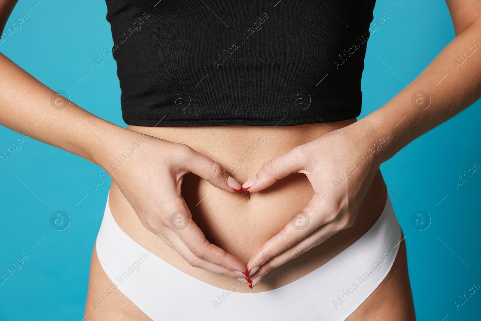Photo of Young woman with flat belly making heart gesture on light blue background, closeup