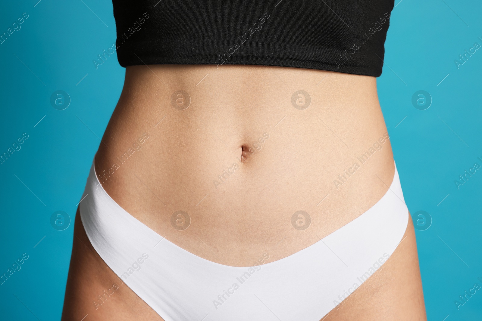 Photo of Young woman with flat belly on light blue background, closeup