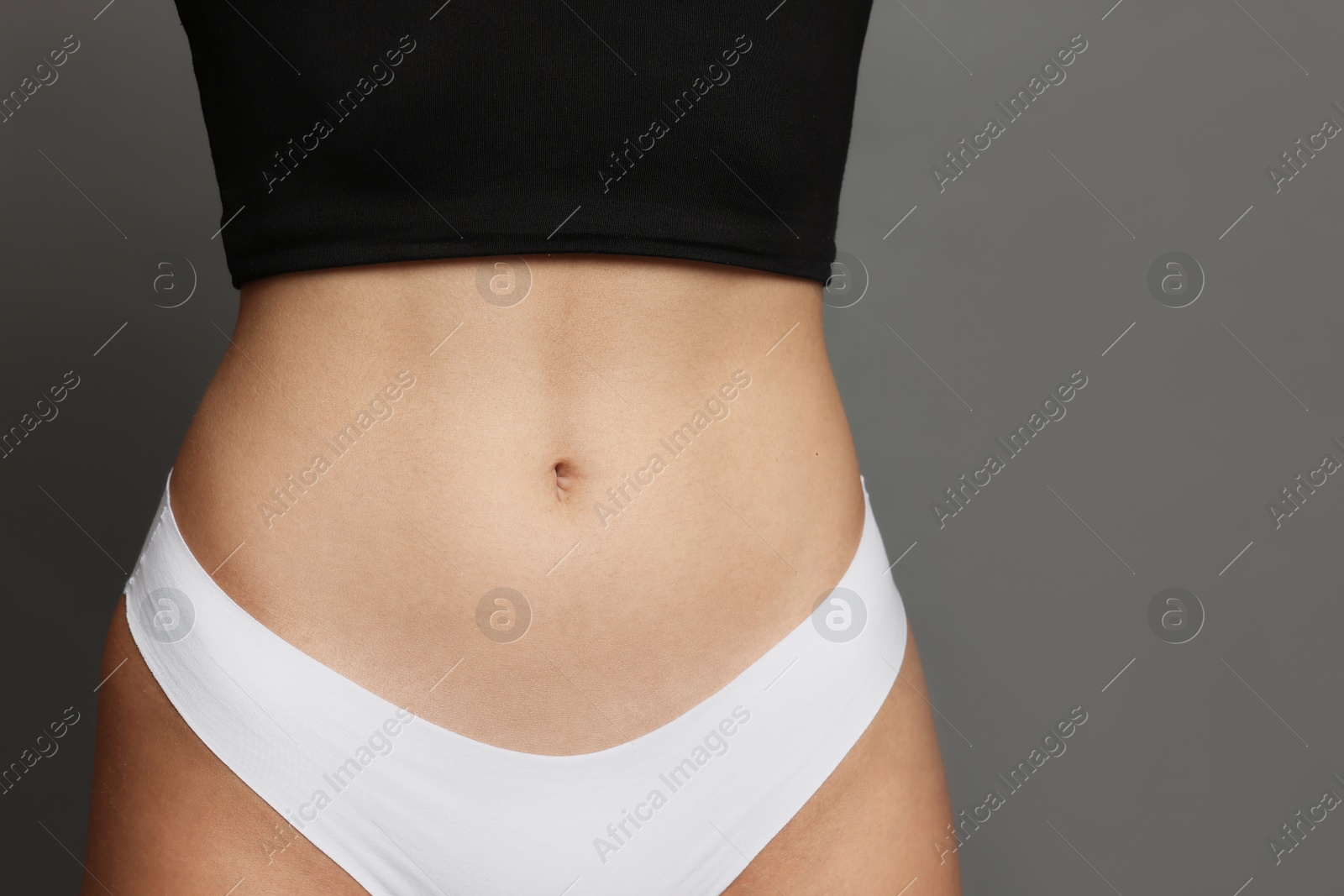 Photo of Young woman with flat belly on grey background, closeup. Space for text