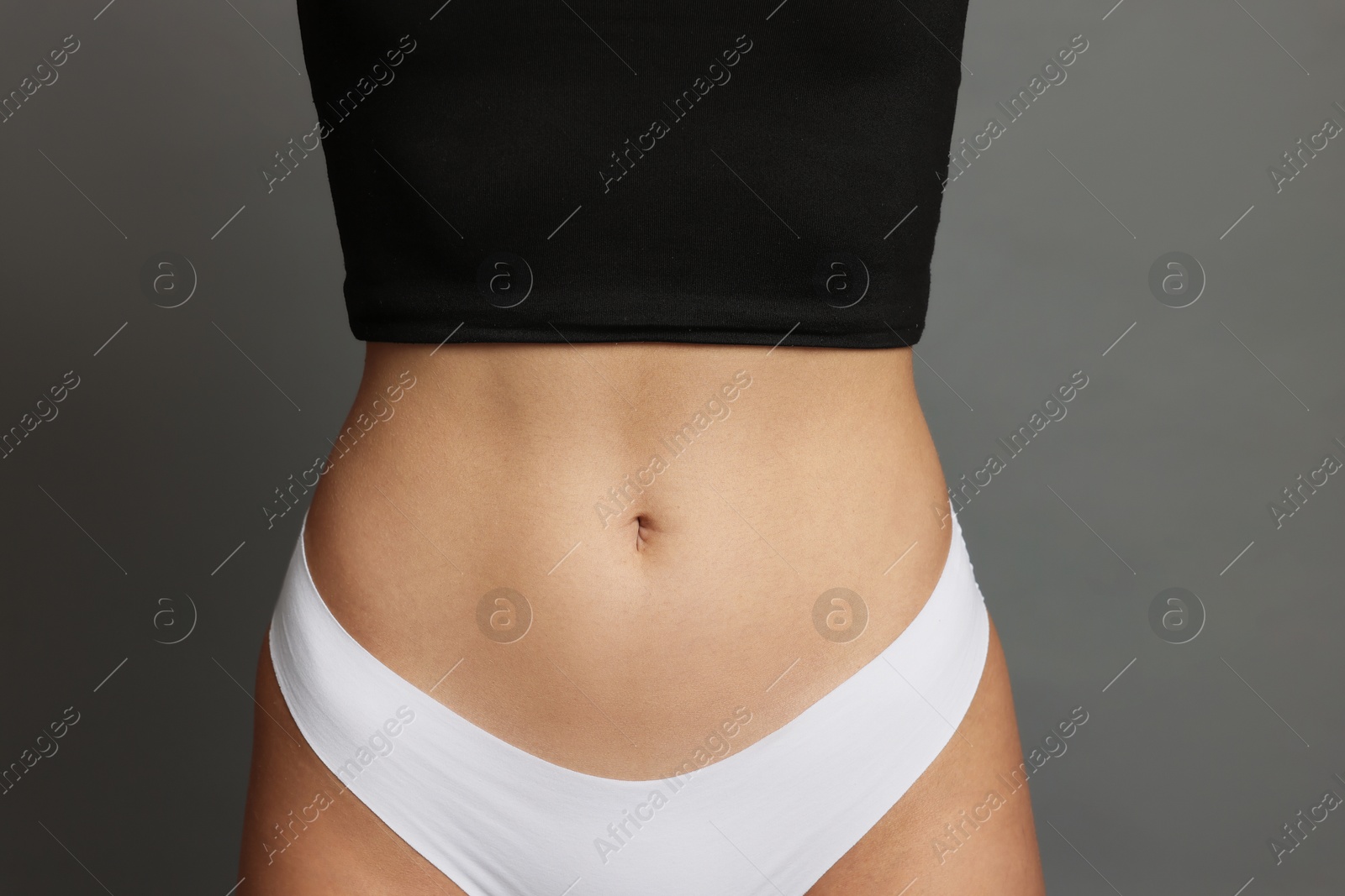 Photo of Young woman with flat belly on grey background, closeup