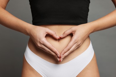 Photo of Young woman with flat belly making heart gesture on grey background, closeup