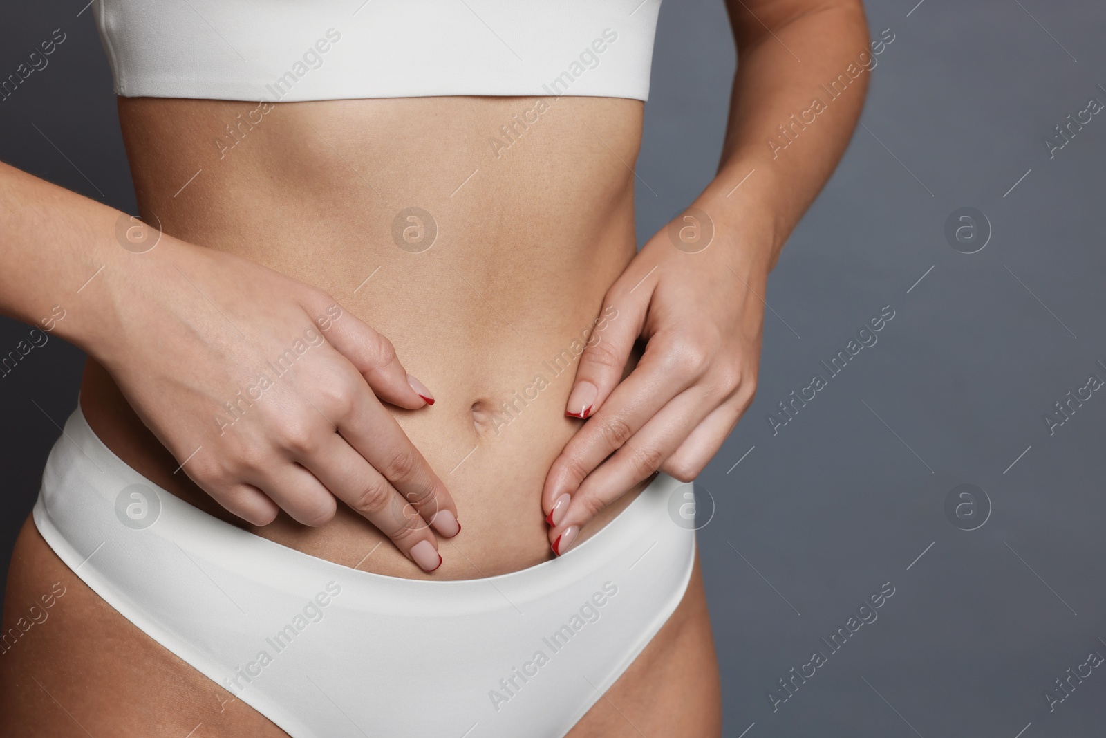 Photo of Young woman with flat belly on grey background, closeup