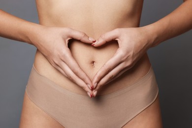 Photo of Young woman with flat belly making heart gesture on grey background, closeup