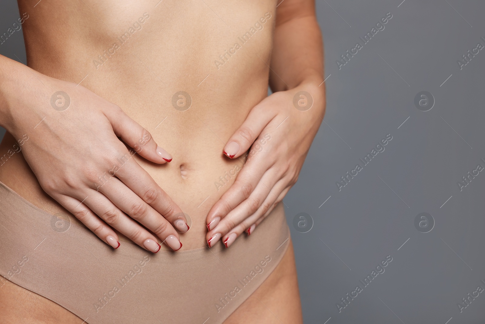 Photo of Young woman with flat belly on grey background, closeup. Space for text
