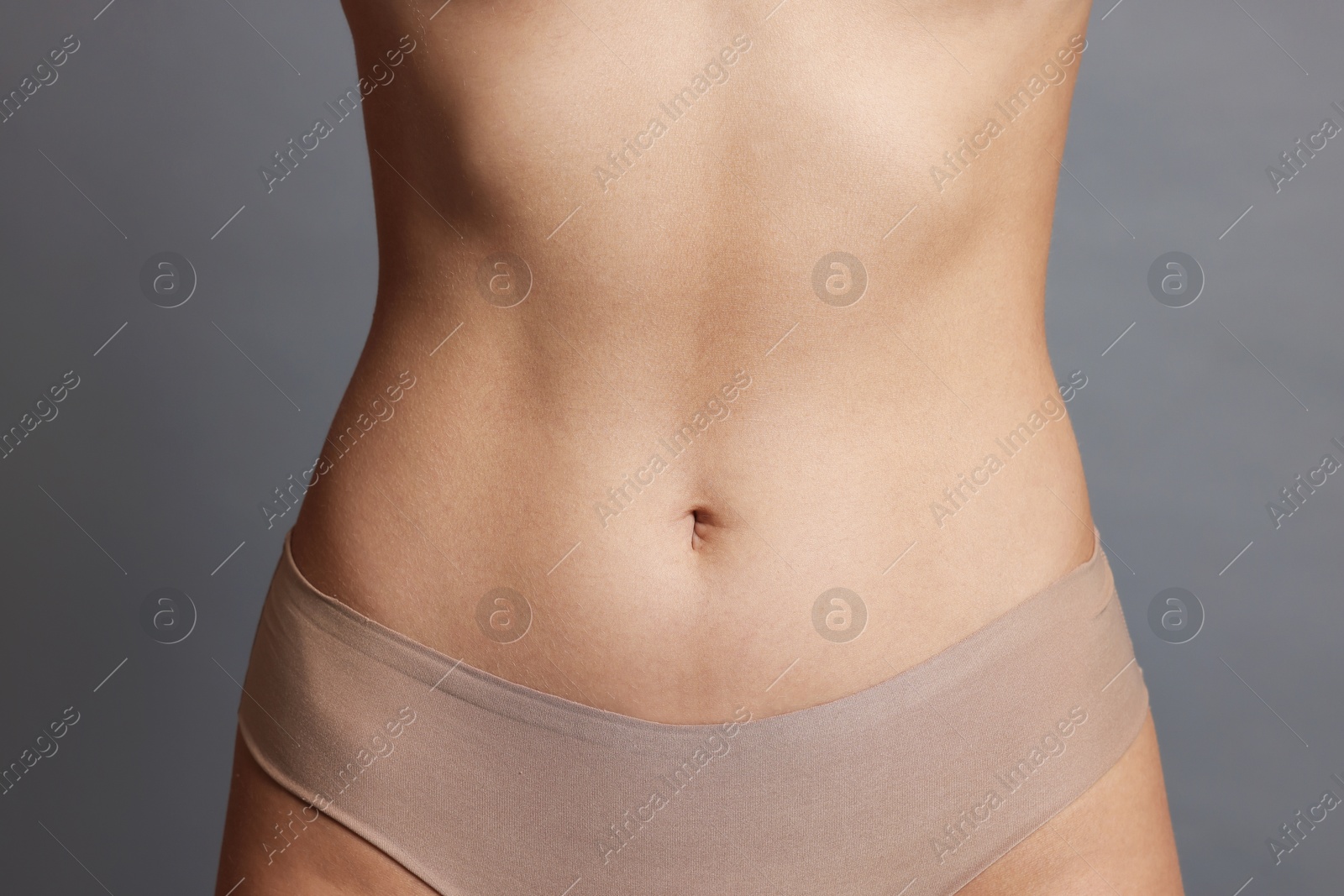 Photo of Young woman with flat belly on grey background, closeup