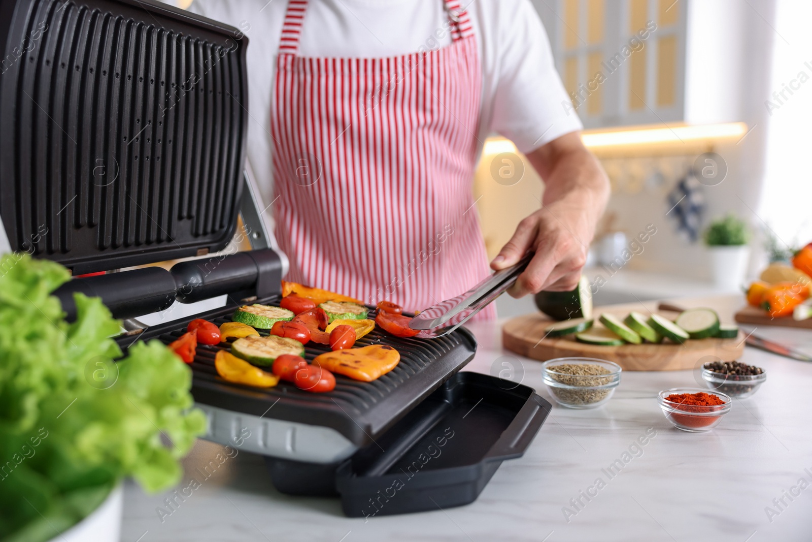 Photo of Man cooking vegetables on electric grill in kitchen, closeup
